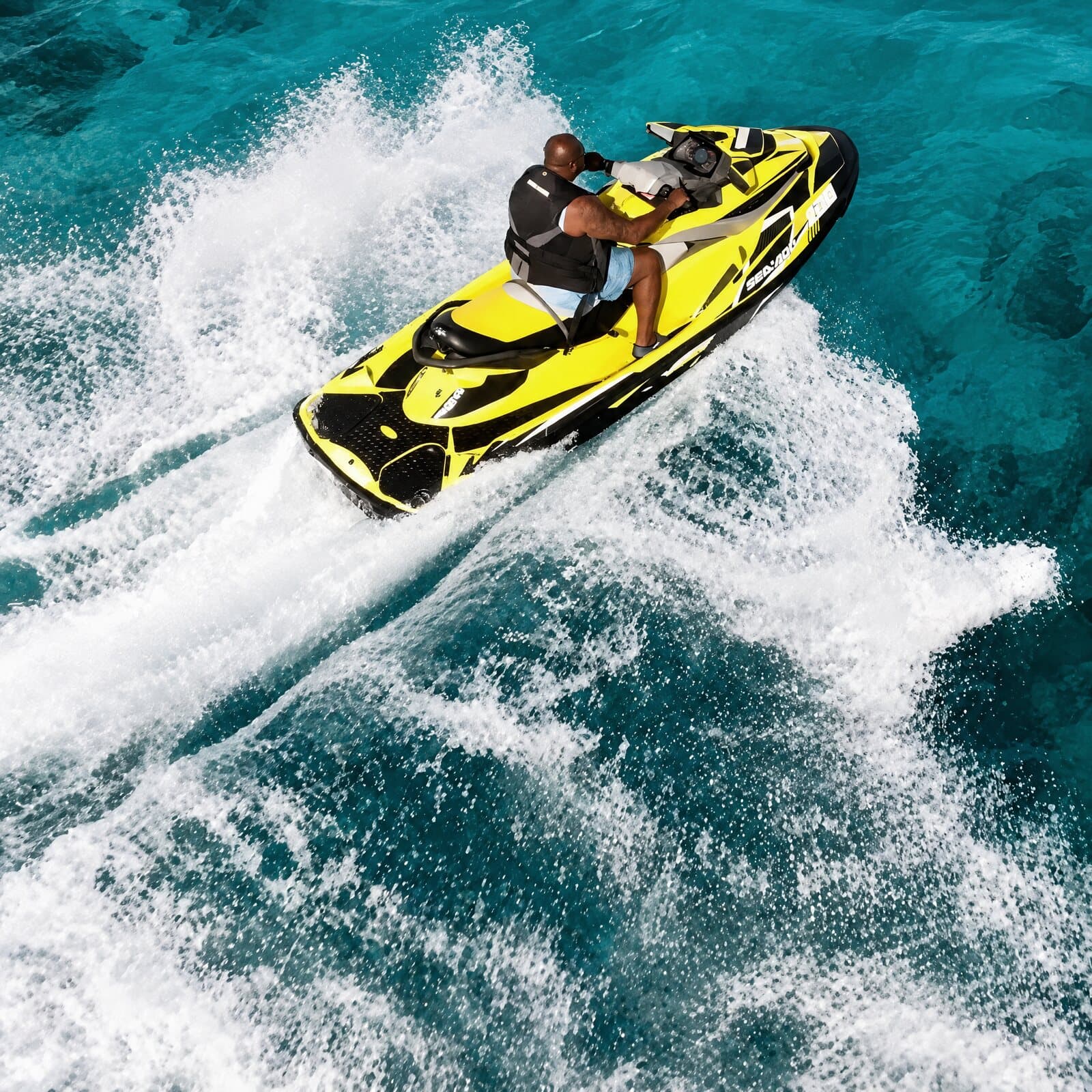 Two people on a yellow jet ski turning in a burst of spray, seen from above