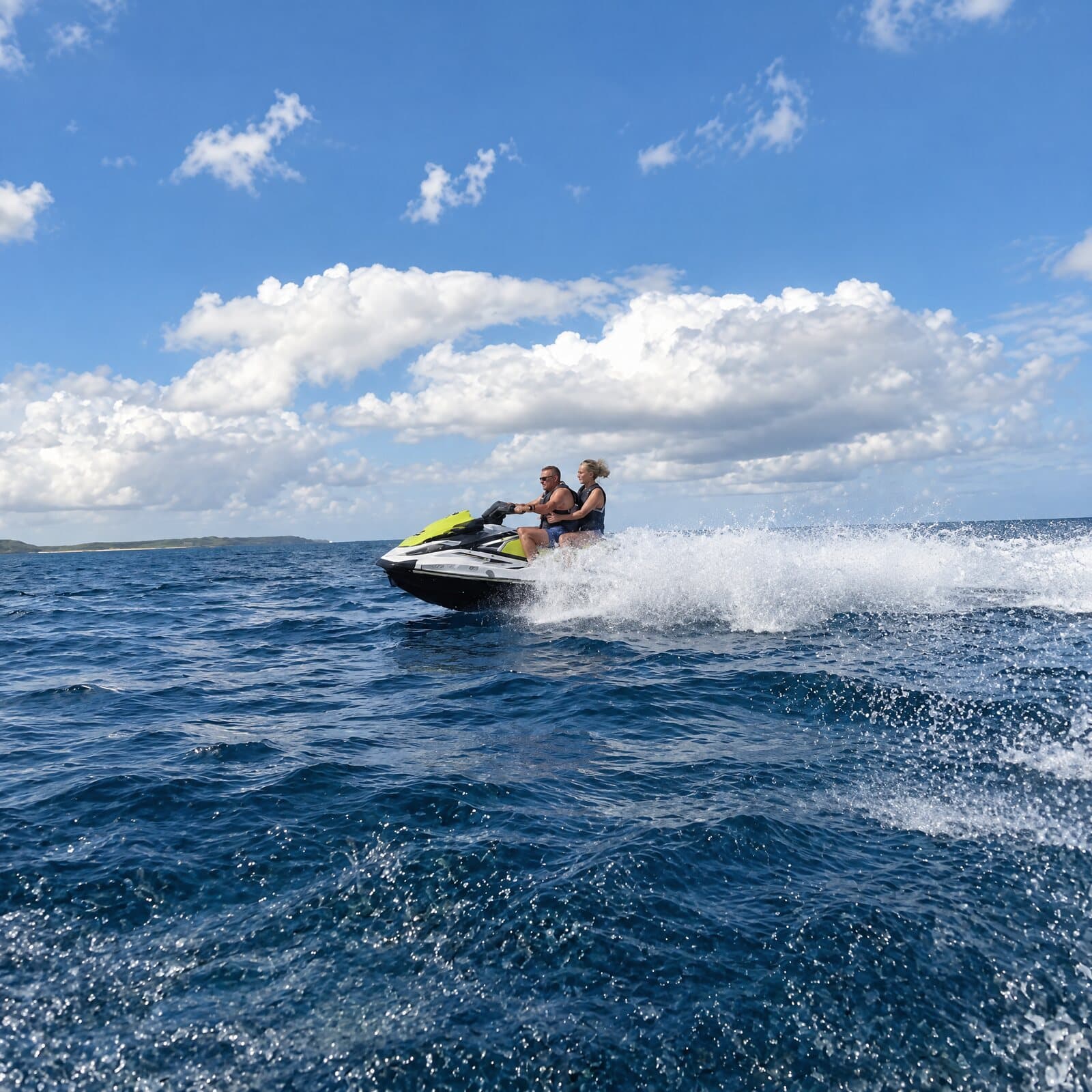 Two people speeding across the open sea on a jet ski, in a burst of spray