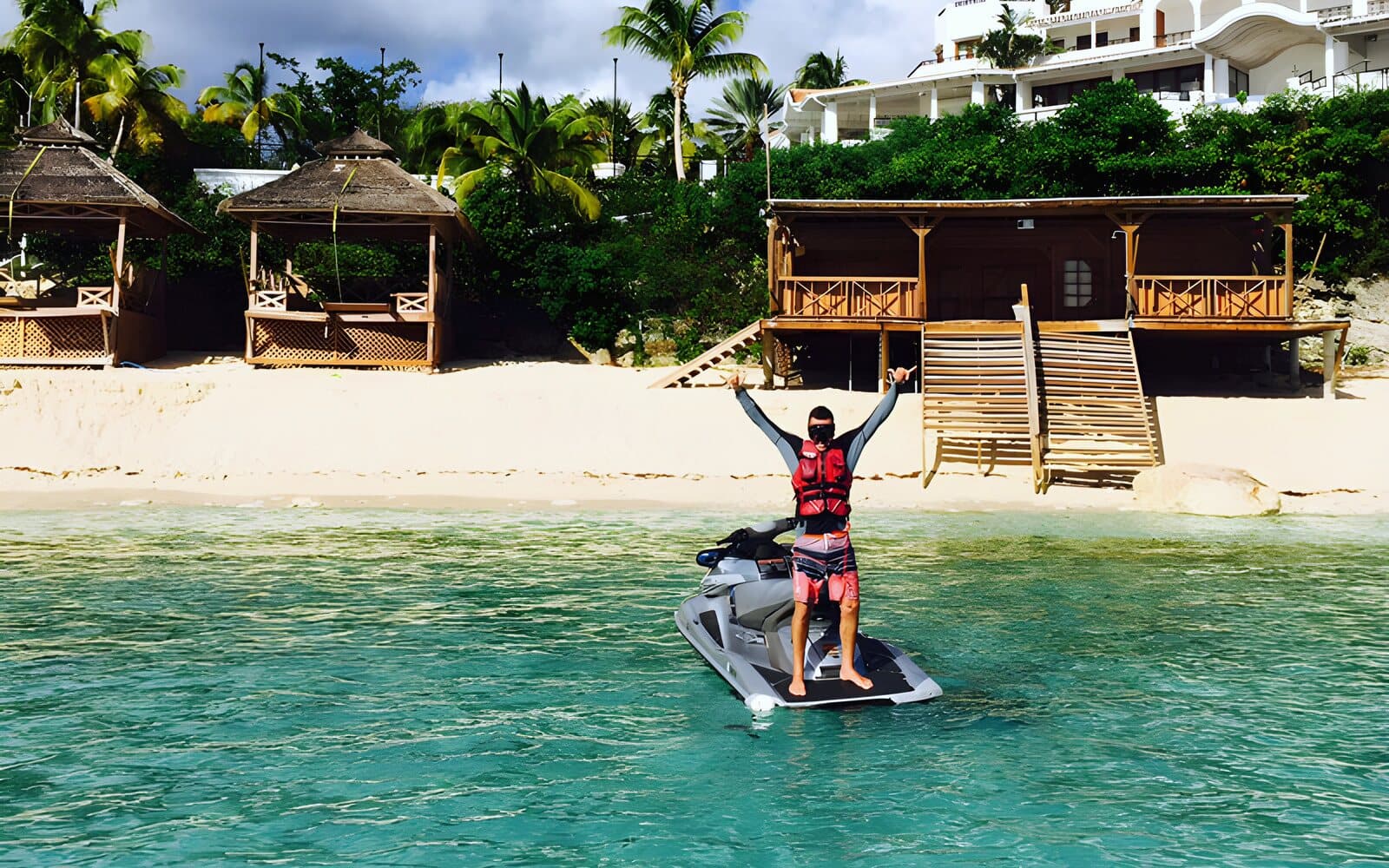 A rider standing on his jet ski, arms raised, in front of La Samanna hotel's beach