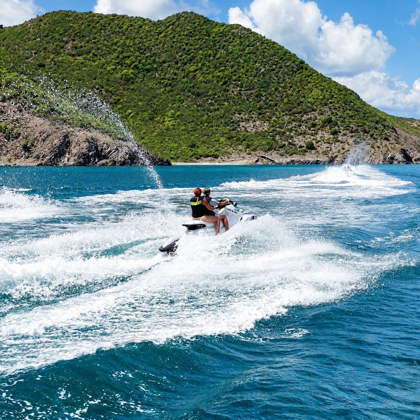 Jet skis speeding through the spray at the foot of a green hill