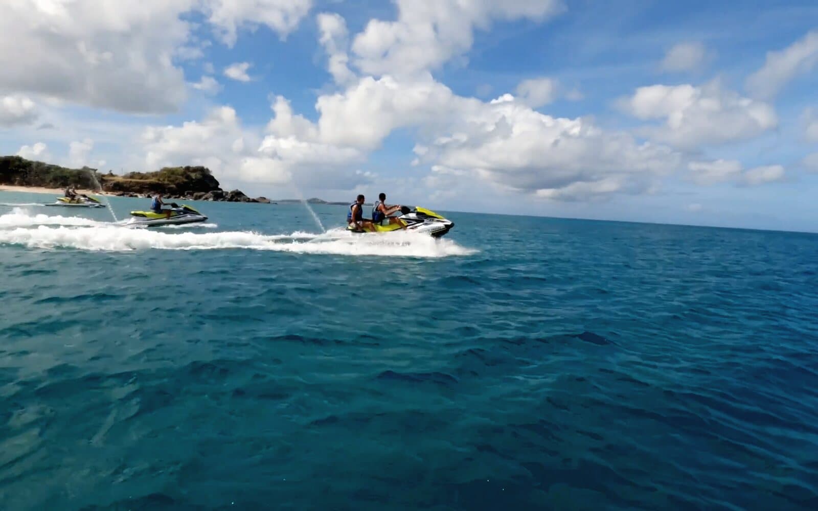 Jet skis at speed on the open sea, two people on the lead one