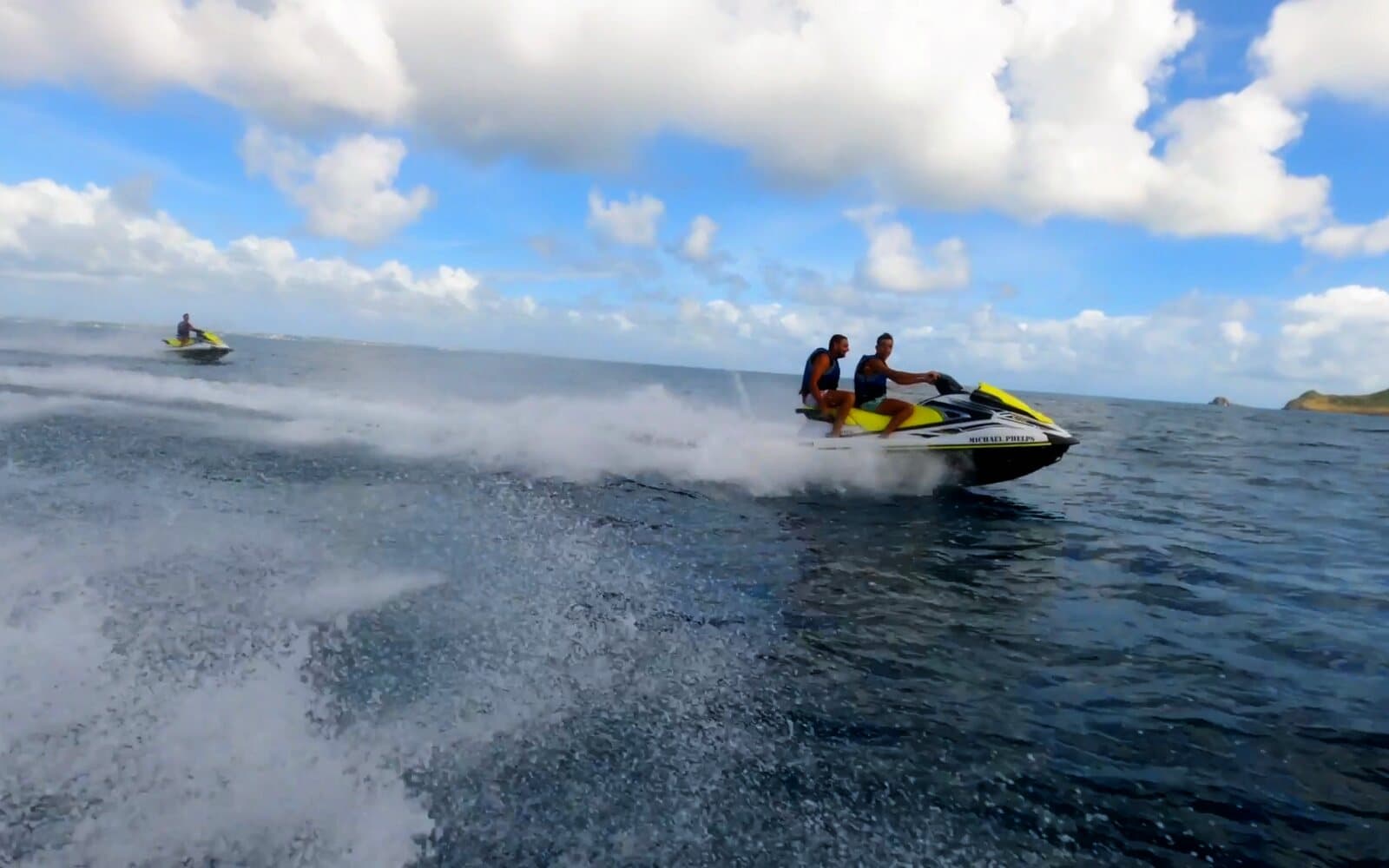Two people on a jet ski at full speed on the open sea, another jet ski in the distance
