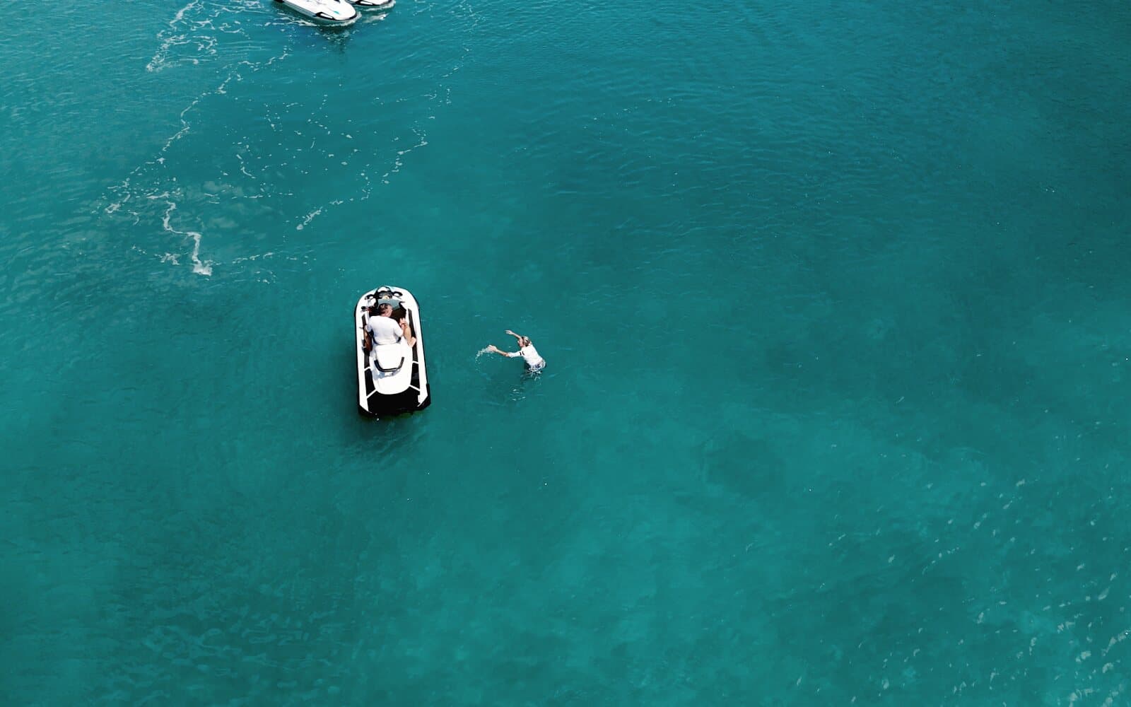 A swimmer beside a stopped jet ski on turquoise water, seen from the drone