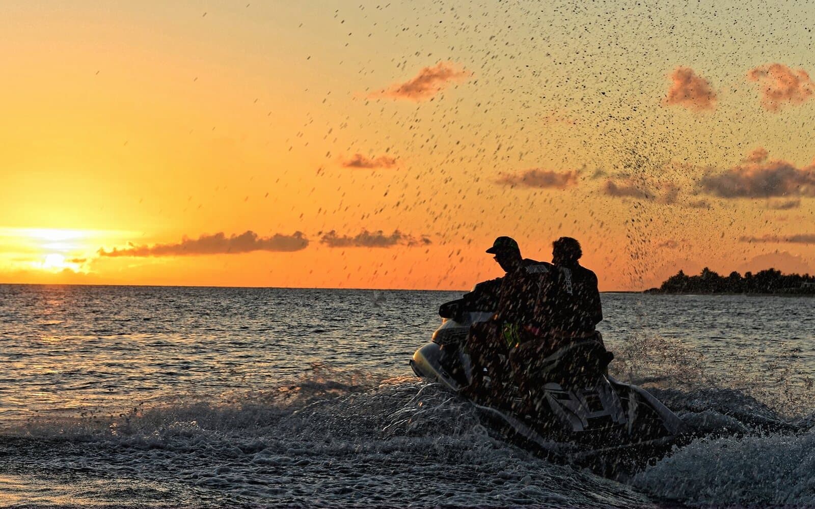Two people on a jet ski in a burst of spray, at sunset