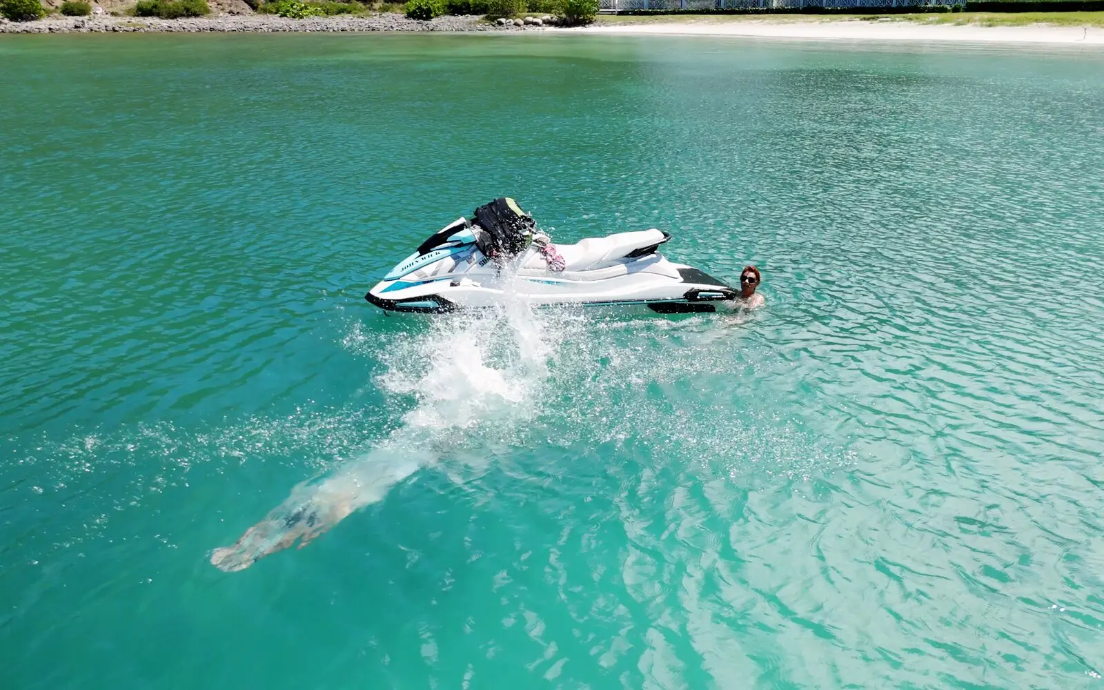 Un bañista se zambulle junto a un jet ski detenido en el agua turquesa, visto desde el dron