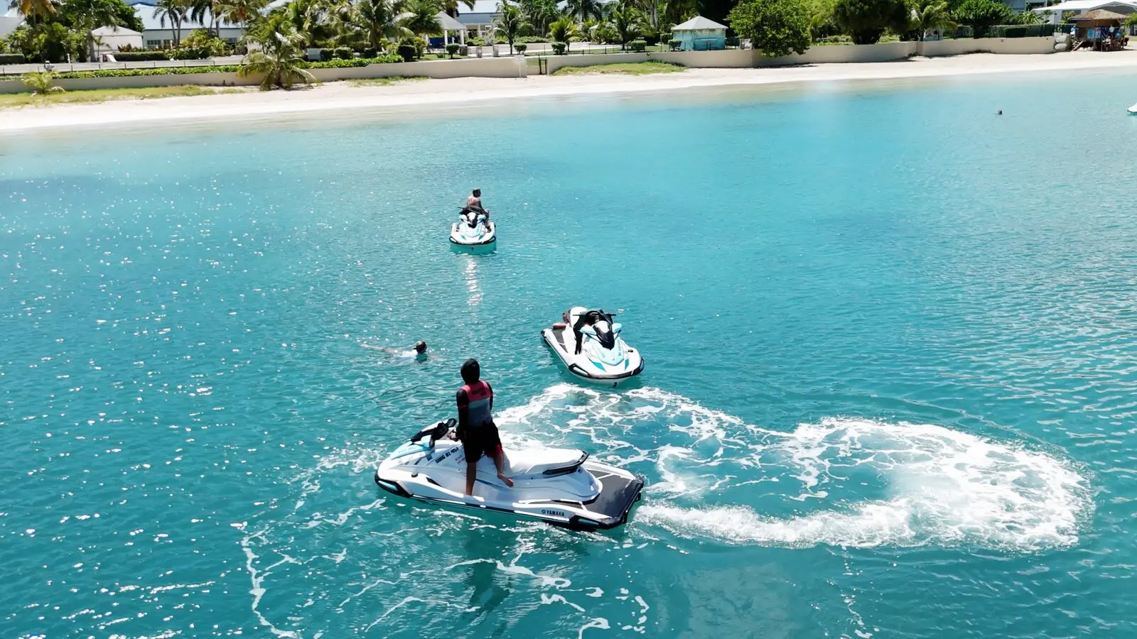 Un jet ski blanc trace une boucle d'écume sur l'eau turquoise, près d'une plage bordée de palmiers