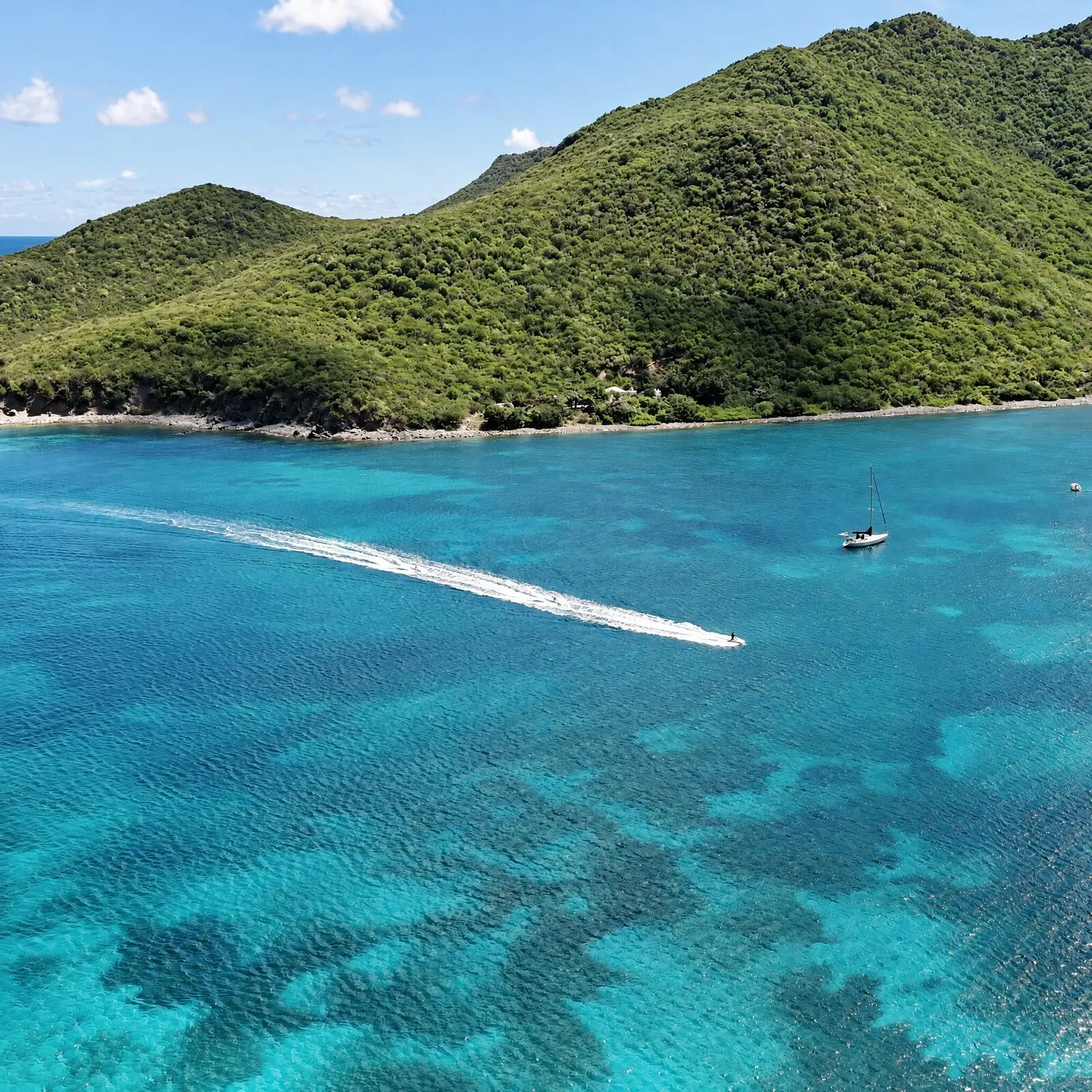Un jet ski avanza a toda velocidad sobre el agua turquesa al pie de una colina verde, visto desde el dron