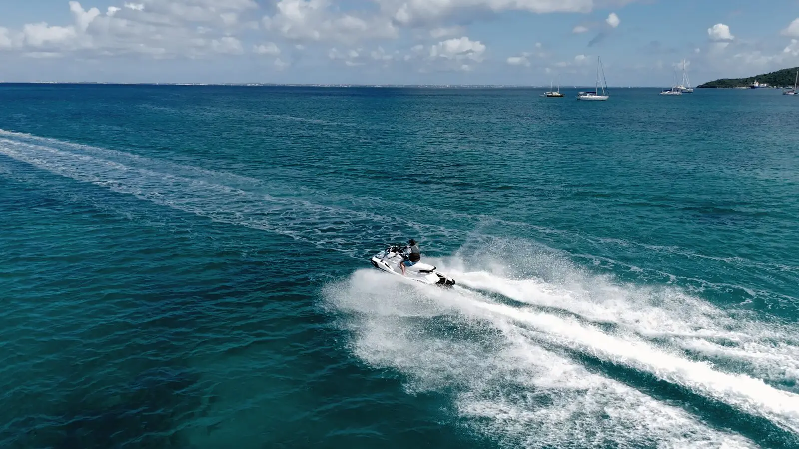 Un pilote seul sur son jet ski soulève une gerbe d'écume en pleine mer, des voiliers au loin