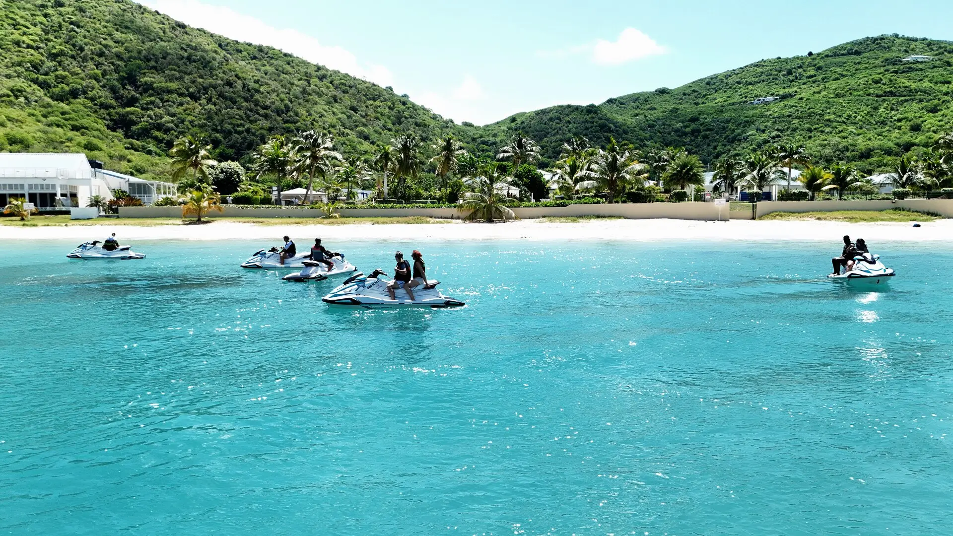 Jet skis detenidos sobre el agua turquesa frente a la playa de Anse Marcel, con las colinas detrás