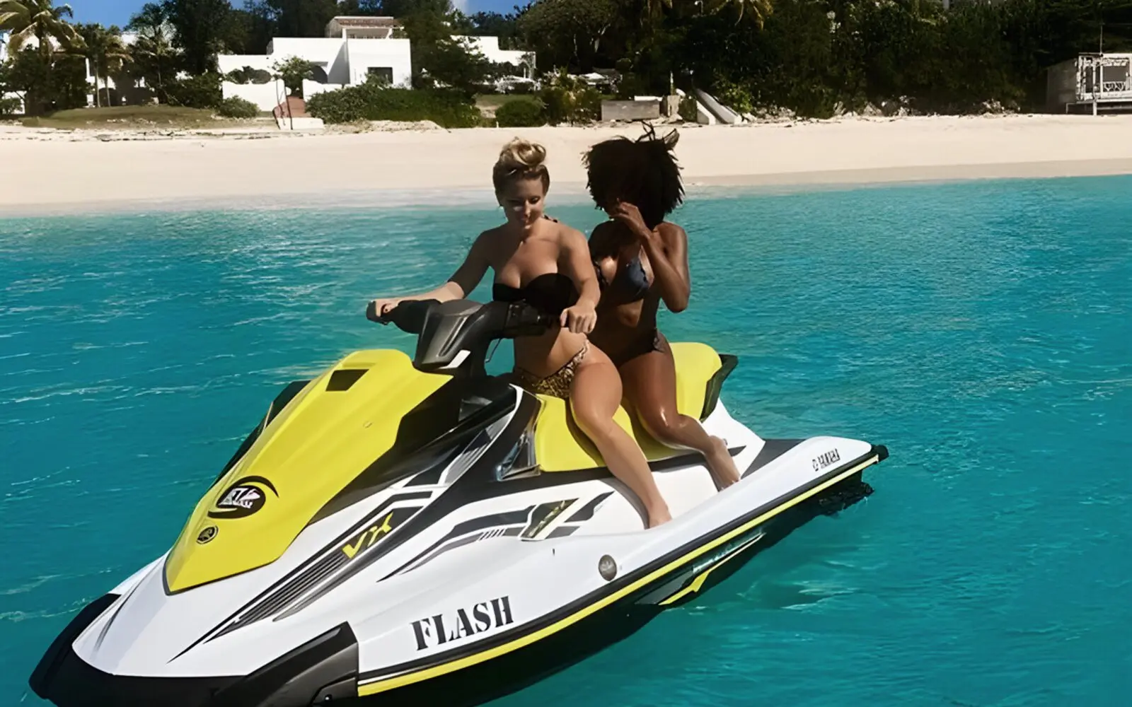 Dos mujeres en un jet ski amarillo, en el agua turquesa frente a una playa