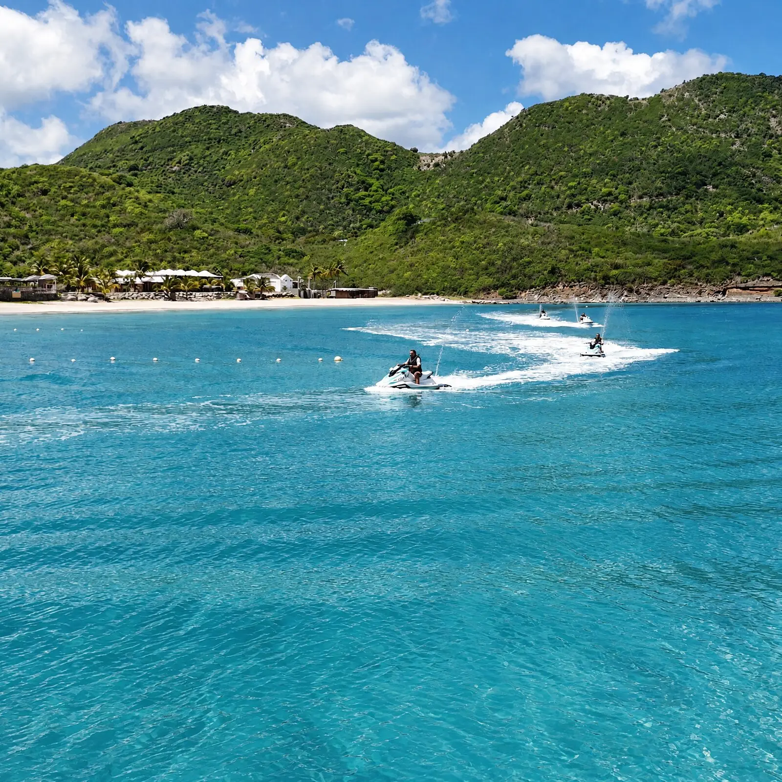 Un jet ski cruza la bahía turquesa de Anse Marcel, frente a la playa y las colinas