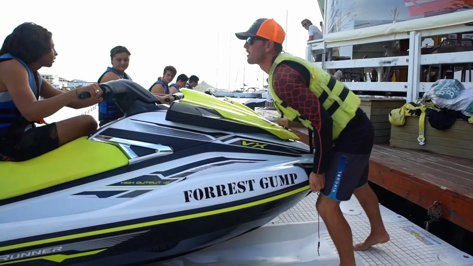 Au ponton, un moniteur en gilet jaune explique le jet ski à des clients en gilet de sauvetage