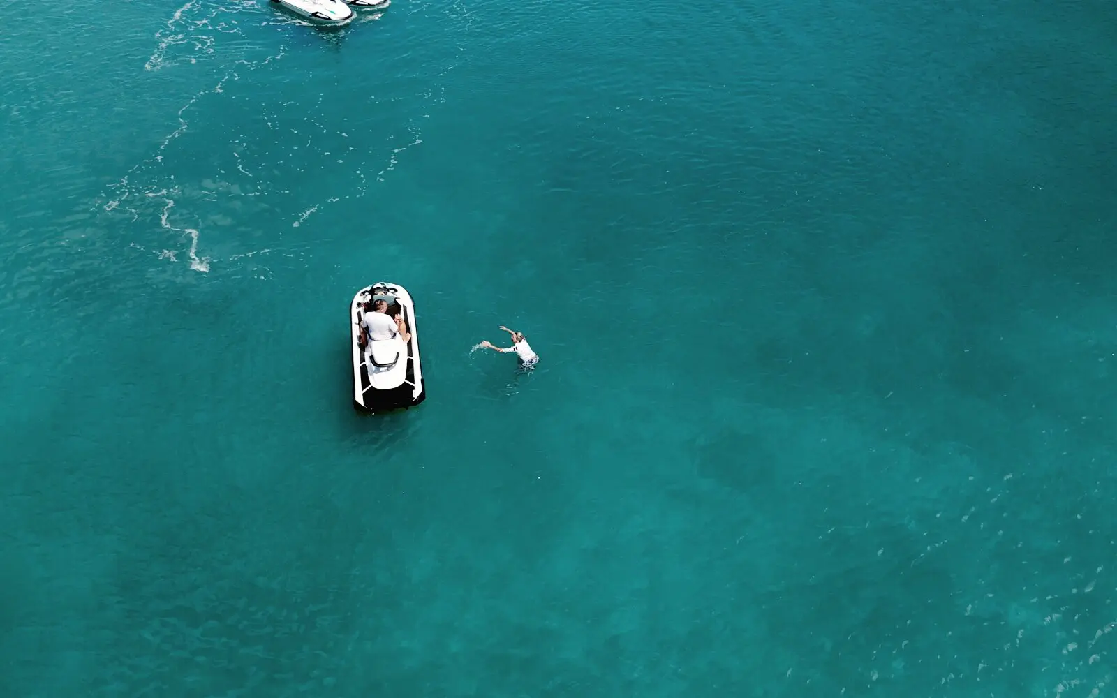 Un nadador junto a su jet ski detenido en el agua turquesa, visto desde el dron